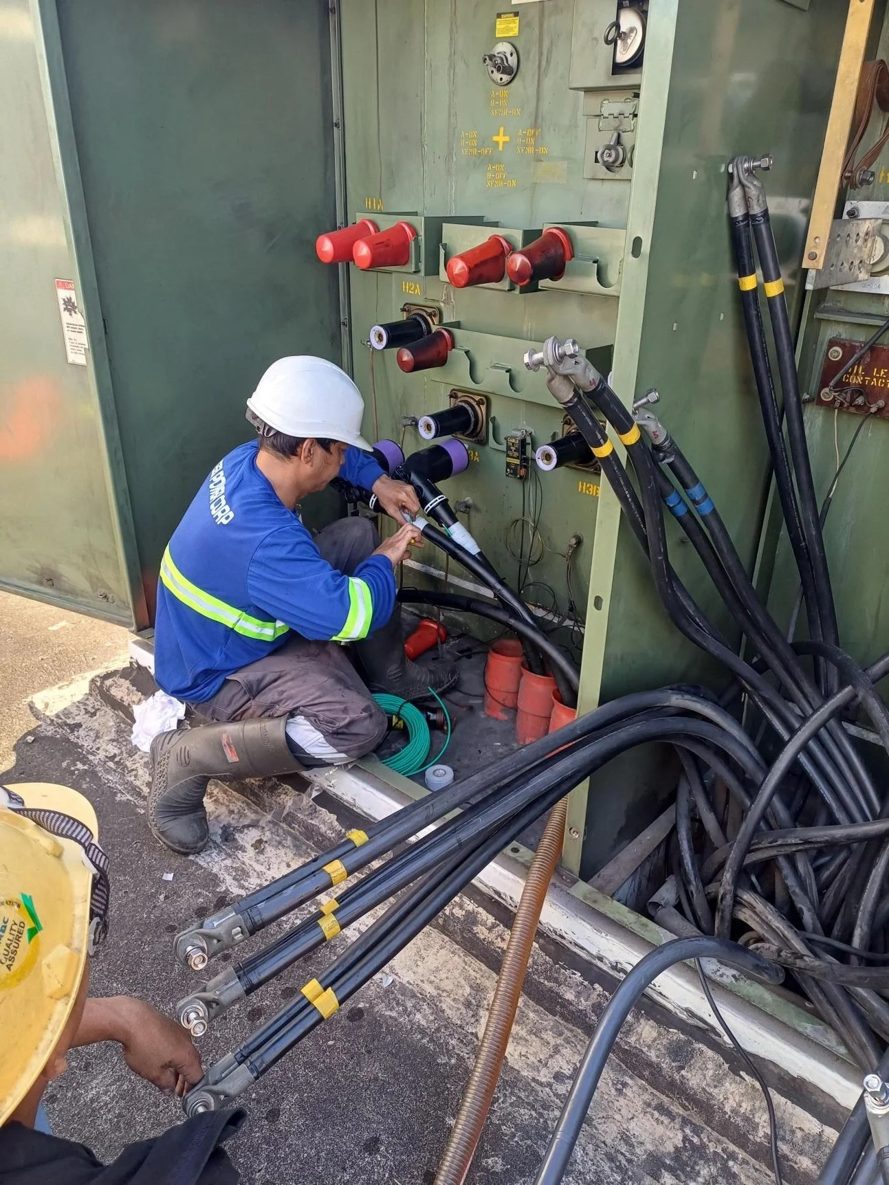 Electrician working on power lines with tools and equipment, wearing a white helmet and safety gear.